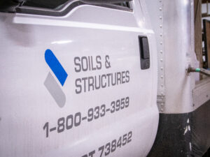 A truck side panel features the Soils & Structures logo and phone number. 